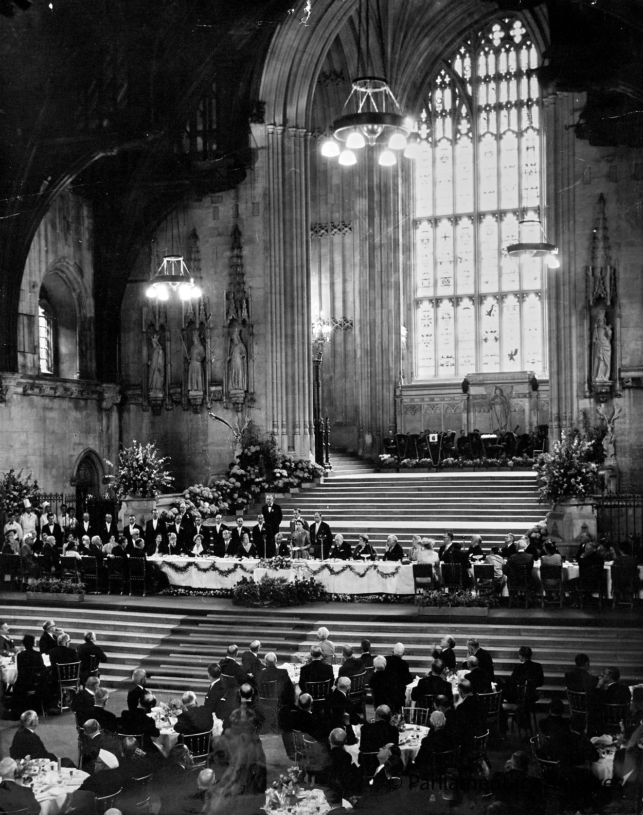 Black and white photograph of Queen Elizabeth II standing on the stairs of Westminster Hall addressing a crowd of people. 